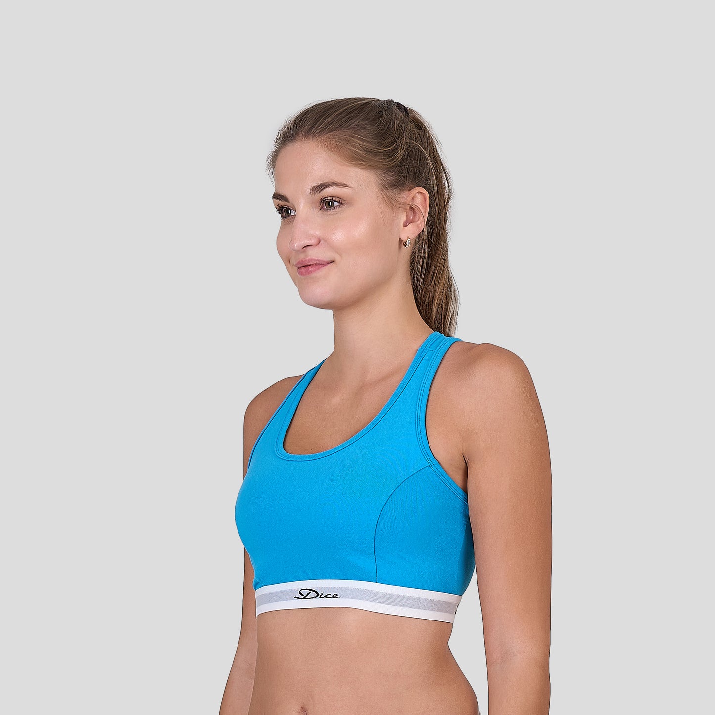 Woman wearing a Dice blue sports bra and white underwear on a light gray background